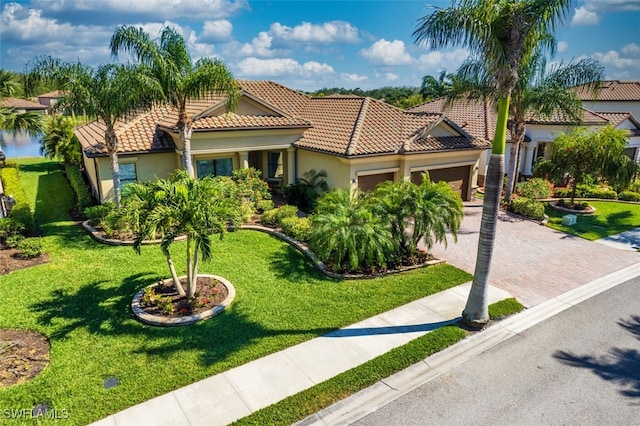 mediterranean / spanish-style home featuring a tile roof, a front yard, a garage, and stucco siding