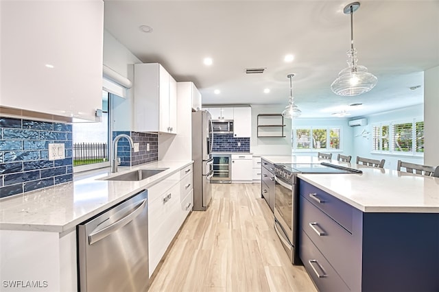 kitchen with a spacious island, a sink, appliances with stainless steel finishes, light wood finished floors, and decorative light fixtures