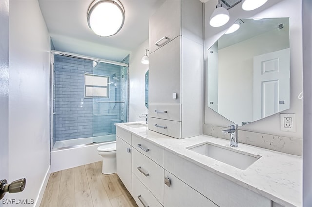 full bathroom featuring bath / shower combo with glass door, wood finished floors, a sink, and toilet