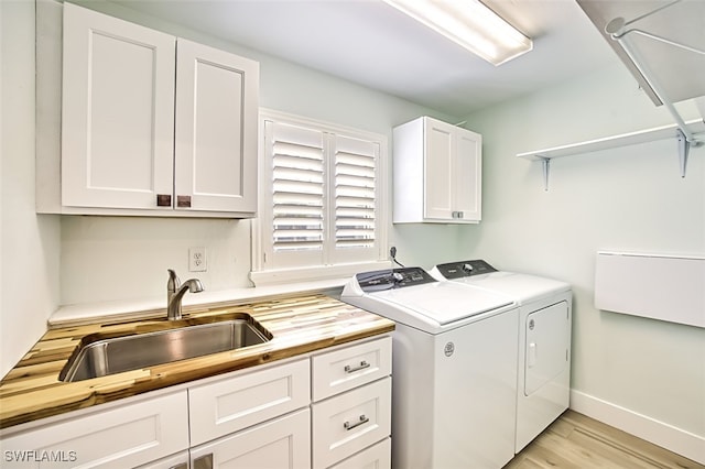 washroom with separate washer and dryer, a sink, baseboards, cabinet space, and light wood finished floors