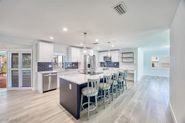 kitchen featuring visible vents, an island with sink, stainless steel appliances, a kitchen bar, and a sink