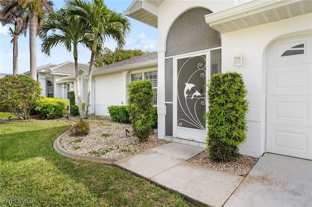 doorway to property featuring an attached garage, a lawn, and stucco siding