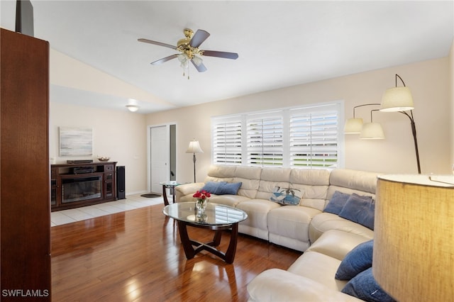 living room featuring a fireplace with flush hearth, a ceiling fan, vaulted ceiling, and wood finished floors