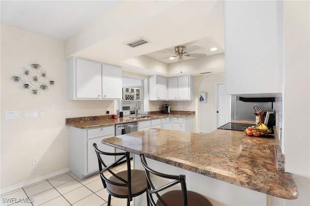 kitchen featuring a raised ceiling, stainless steel dishwasher, a sink, ceiling fan, and a peninsula