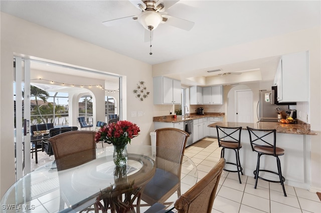 dining room featuring arched walkways, ceiling fan, light tile patterned flooring, visible vents, and a tray ceiling