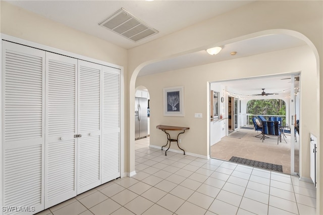 hallway with arched walkways, visible vents, baseboards, and light tile patterned floors