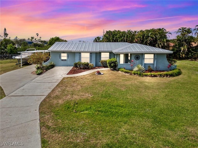 ranch-style home with stucco siding, metal roof, concrete driveway, and a front yard