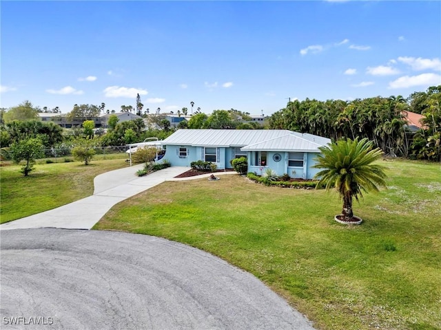 view of front of home with a front lawn, concrete driveway, fence, and metal roof