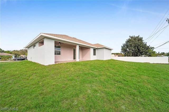 rear view of house with fence, a lawn, a ceiling fan, and stucco siding