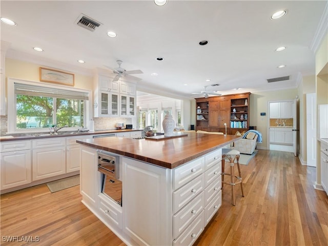 kitchen featuring visible vents, butcher block counters, a kitchen island, ornamental molding, and a kitchen breakfast bar