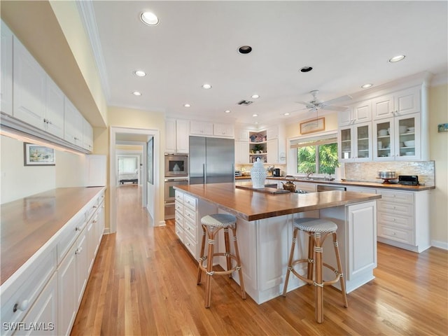 kitchen featuring appliances with stainless steel finishes, white cabinetry, wooden counters, and light wood finished floors