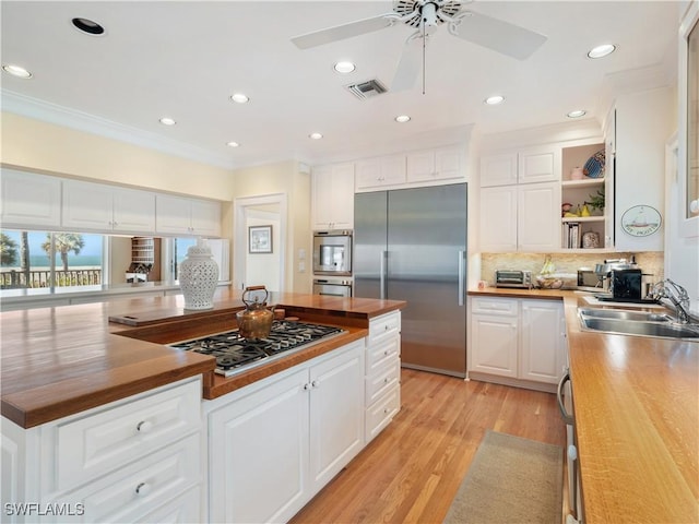 kitchen featuring stainless steel appliances, butcher block counters, a sink, and open shelves