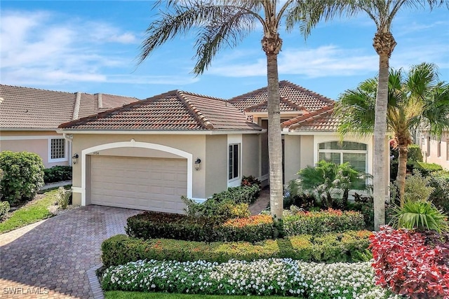 mediterranean / spanish-style home with stucco siding, a tile roof, decorative driveway, and a garage