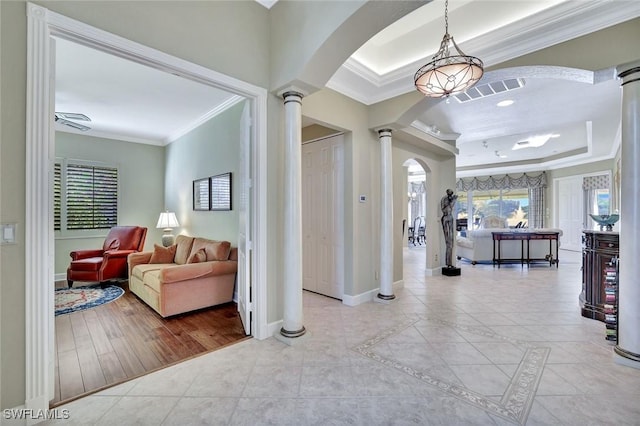 corridor with a raised ceiling, crown molding, tile patterned flooring, and ornate columns