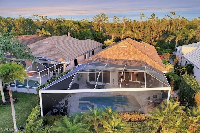 rear view of house with glass enclosure, an outdoor pool, and a patio