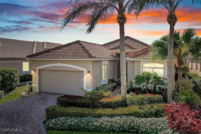 mediterranean / spanish-style home with stucco siding, decorative driveway, an attached garage, and a tile roof