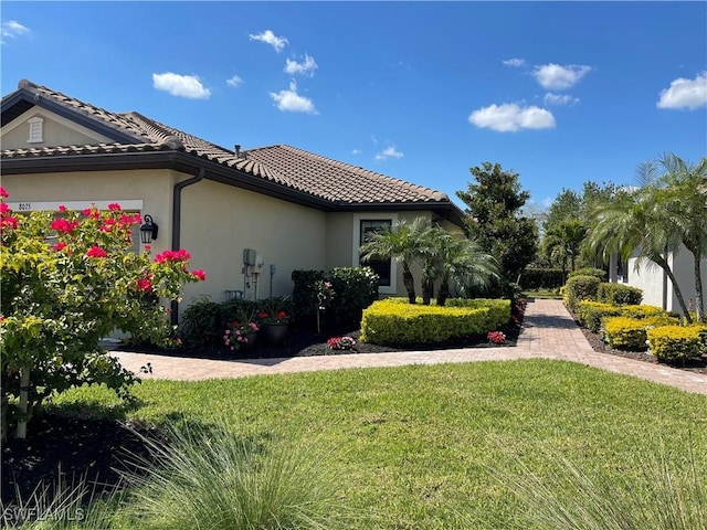 view of property exterior featuring a tile roof, a lawn, a garage, and stucco siding