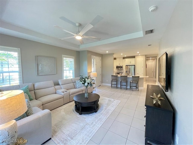 living area with a tray ceiling, visible vents, a healthy amount of sunlight, and light tile patterned floors