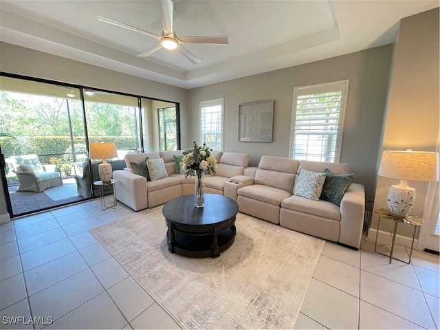 living area with a raised ceiling, light tile patterned floors, baseboards, and ceiling fan