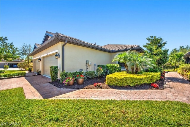 view of home's exterior featuring a tiled roof, stucco siding, an attached garage, and decorative driveway