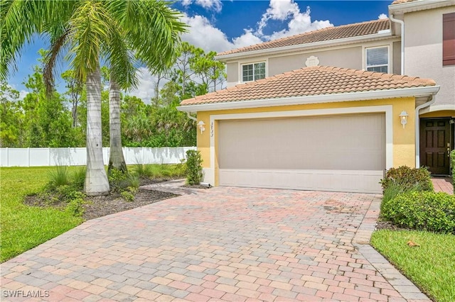 view of front of house with a garage, a tile roof, fence, decorative driveway, and stucco siding