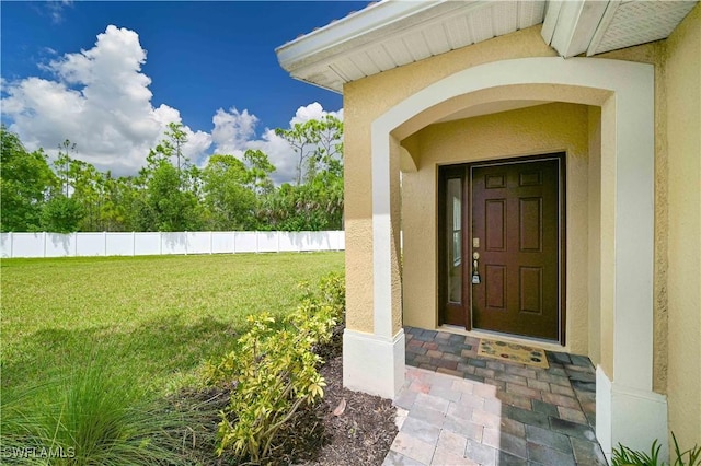 property entrance featuring a yard, fence, and stucco siding