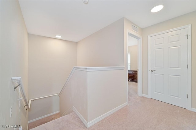 hall with carpet, visible vents, baseboards, and an upstairs landing