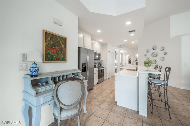 kitchen featuring visible vents, a breakfast bar, a sink, stainless steel appliances, and white cabinetry