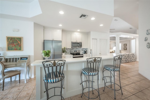 kitchen featuring visible vents, decorative backsplash, a kitchen breakfast bar, stainless steel appliances, and ornate columns