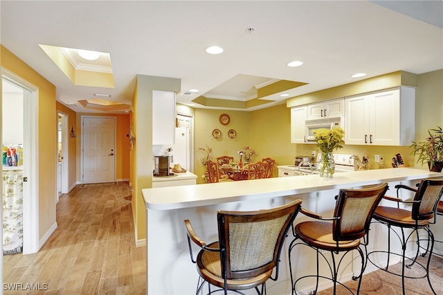 kitchen featuring ornamental molding, white cabinetry, light wood-type flooring, white appliances, and a kitchen bar