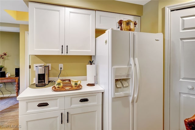 kitchen with white fridge with ice dispenser, light wood finished floors, light countertops, and white cabinets