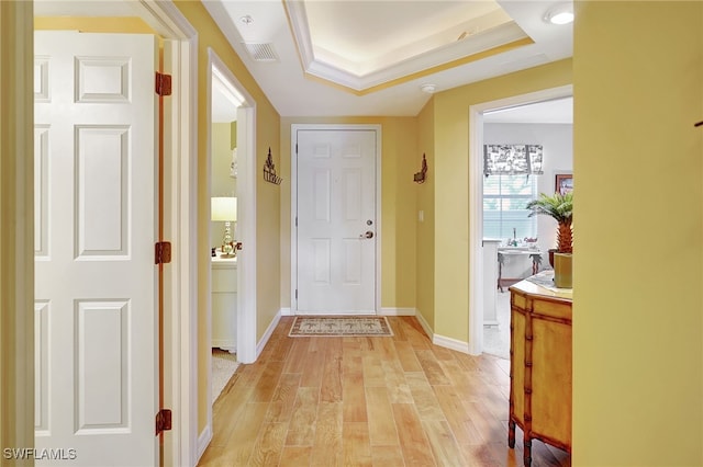 interior space with baseboards, a raised ceiling, visible vents, and light wood-style floors