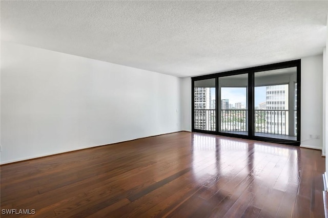 spare room with a textured ceiling, a city view, wood finished floors, and floor to ceiling windows