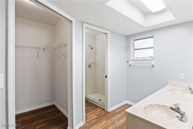 full bath featuring tiled shower, a sink, a spacious closet, and wood finished floors