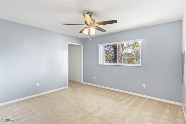 empty room with baseboards, a ceiling fan, and light colored carpet