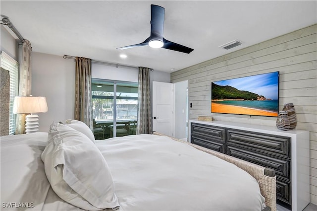 bedroom with access to outside, visible vents, wood walls, and ceiling fan