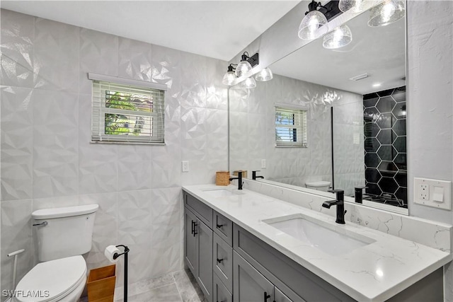 bathroom with toilet, double vanity, tile walls, and a sink