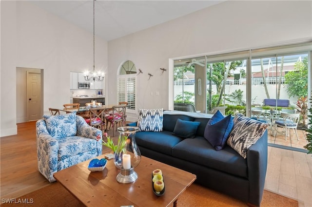 living room with light wood-style floors, baseboards, a notable chandelier, and high vaulted ceiling