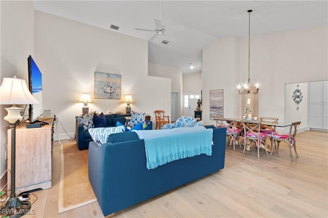 living area featuring light wood finished floors, visible vents, baseboards, ceiling fan with notable chandelier, and high vaulted ceiling