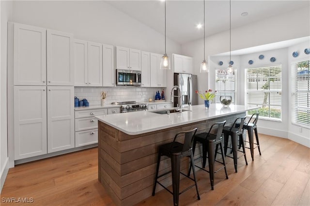 kitchen with a breakfast bar area, an island with sink, a sink, appliances with stainless steel finishes, and backsplash