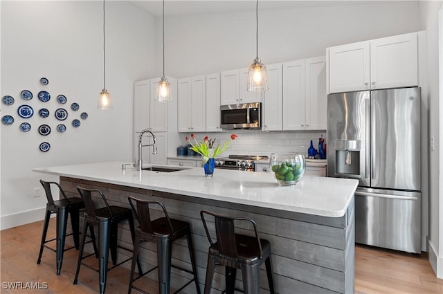 kitchen featuring a sink, stainless steel appliances, light wood-type flooring, and an island with sink