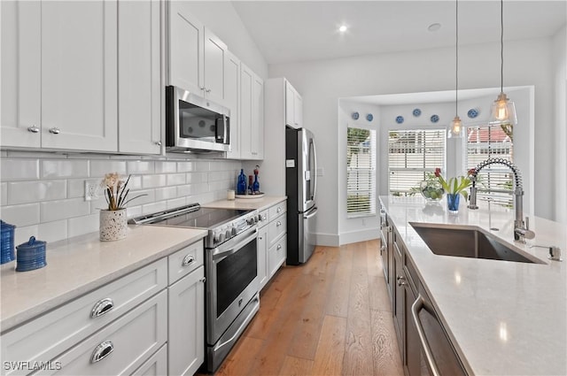 kitchen featuring light wood-type flooring, a sink, decorative light fixtures, appliances with stainless steel finishes, and decorative backsplash