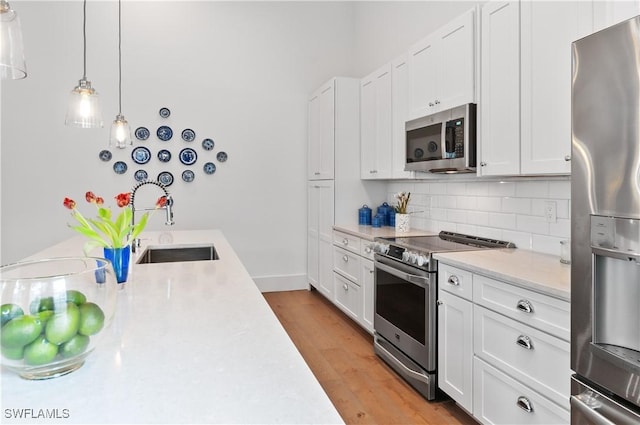 kitchen with light wood finished floors, backsplash, light countertops, appliances with stainless steel finishes, and white cabinets