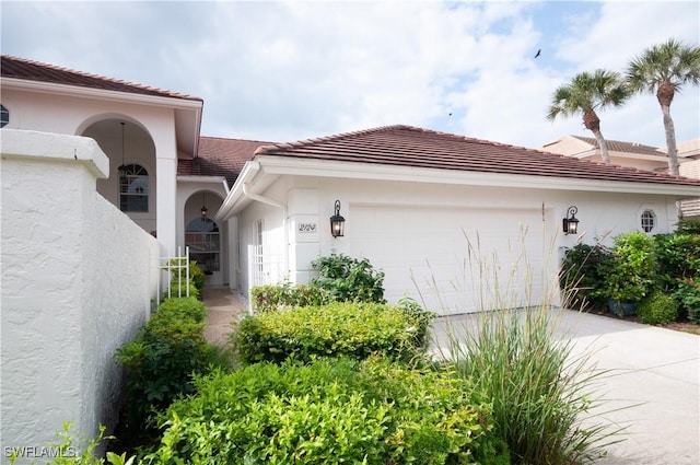 view of side of property featuring a garage, a tile roof, concrete driveway, and stucco siding