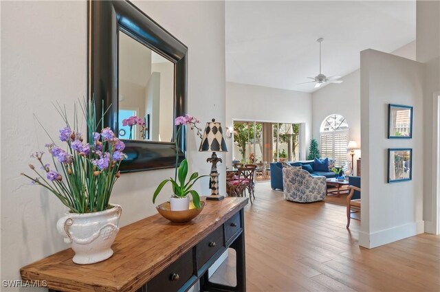 hallway with high vaulted ceiling, baseboards, and wood finished floors