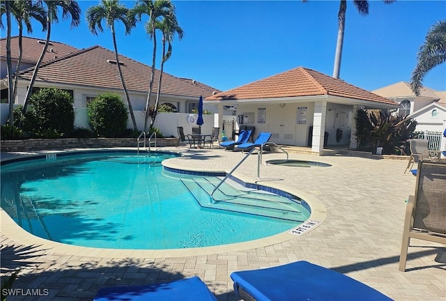 pool with a patio area, a community hot tub, and fence