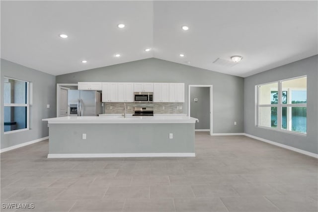 kitchen with stainless steel appliances, white cabinets, vaulted ceiling, light countertops, and a large island with sink