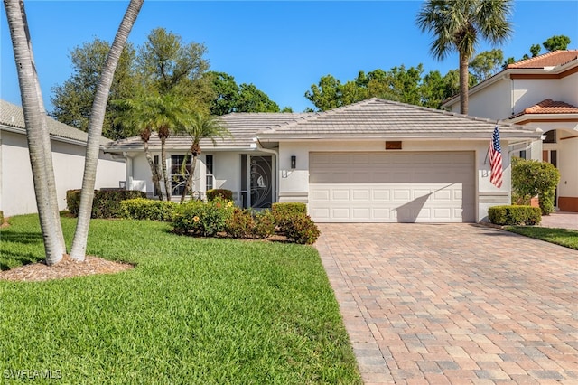 ranch-style home featuring an attached garage, a tile roof, decorative driveway, stucco siding, and a front yard