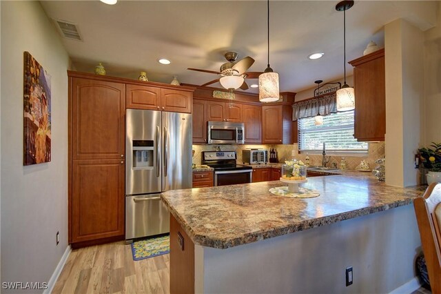 kitchen with brown cabinets, a sink, backsplash, stainless steel appliances, and a peninsula