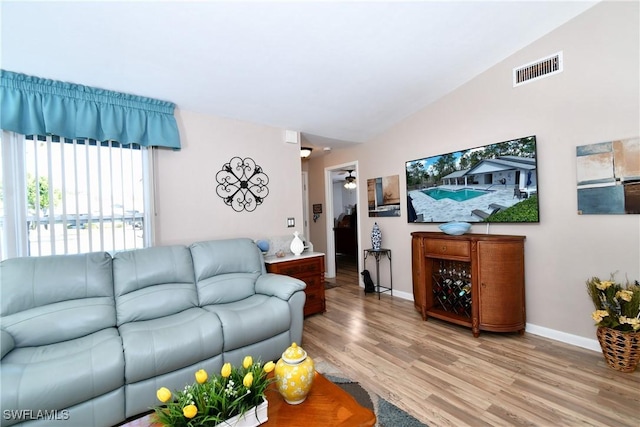 living room with visible vents, baseboards, lofted ceiling, light wood-style flooring, and a ceiling fan